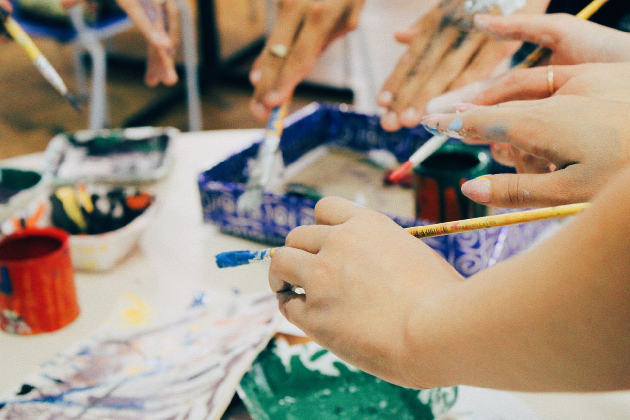 Group of hands holding paintbrushes in a vibrant art workshop, encouraging creativity.