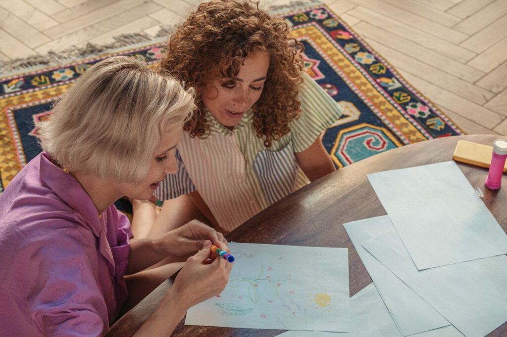 Two women enjoying a creative drawing session indoors with colorful markers and papers.
